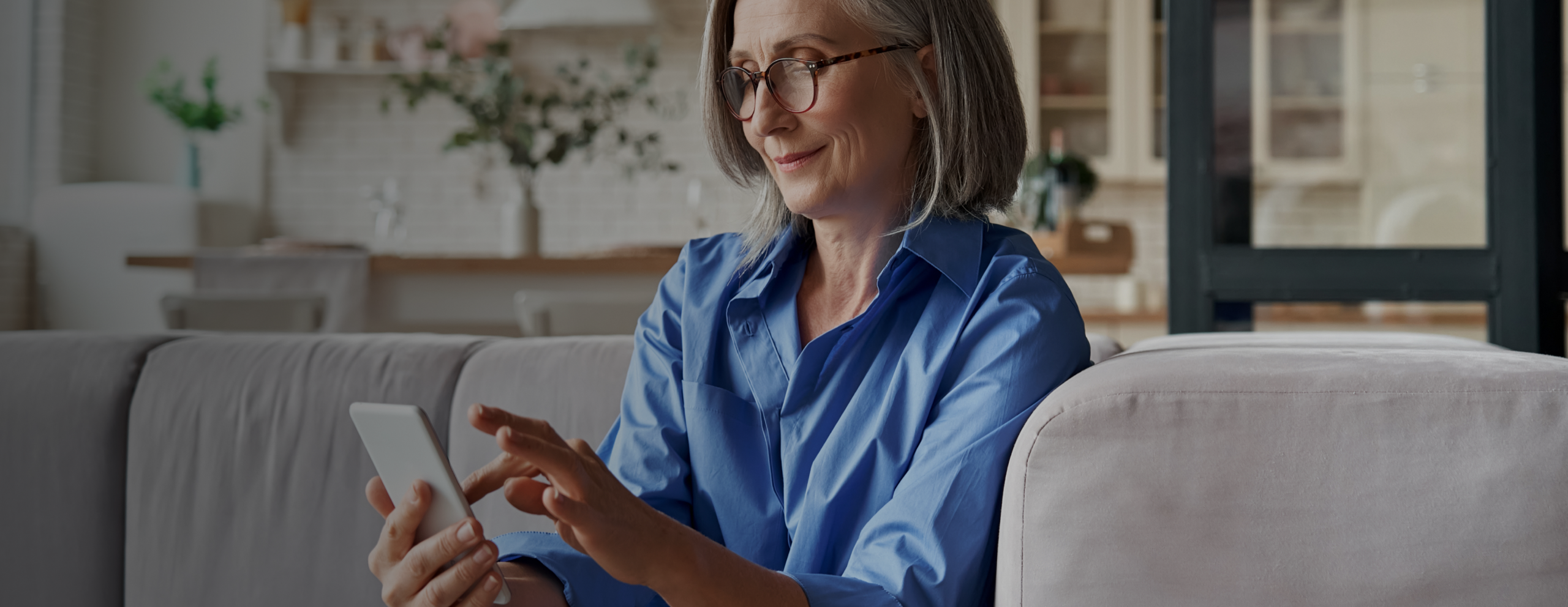 Older woman with glasses sitting on couch interacting with her phone